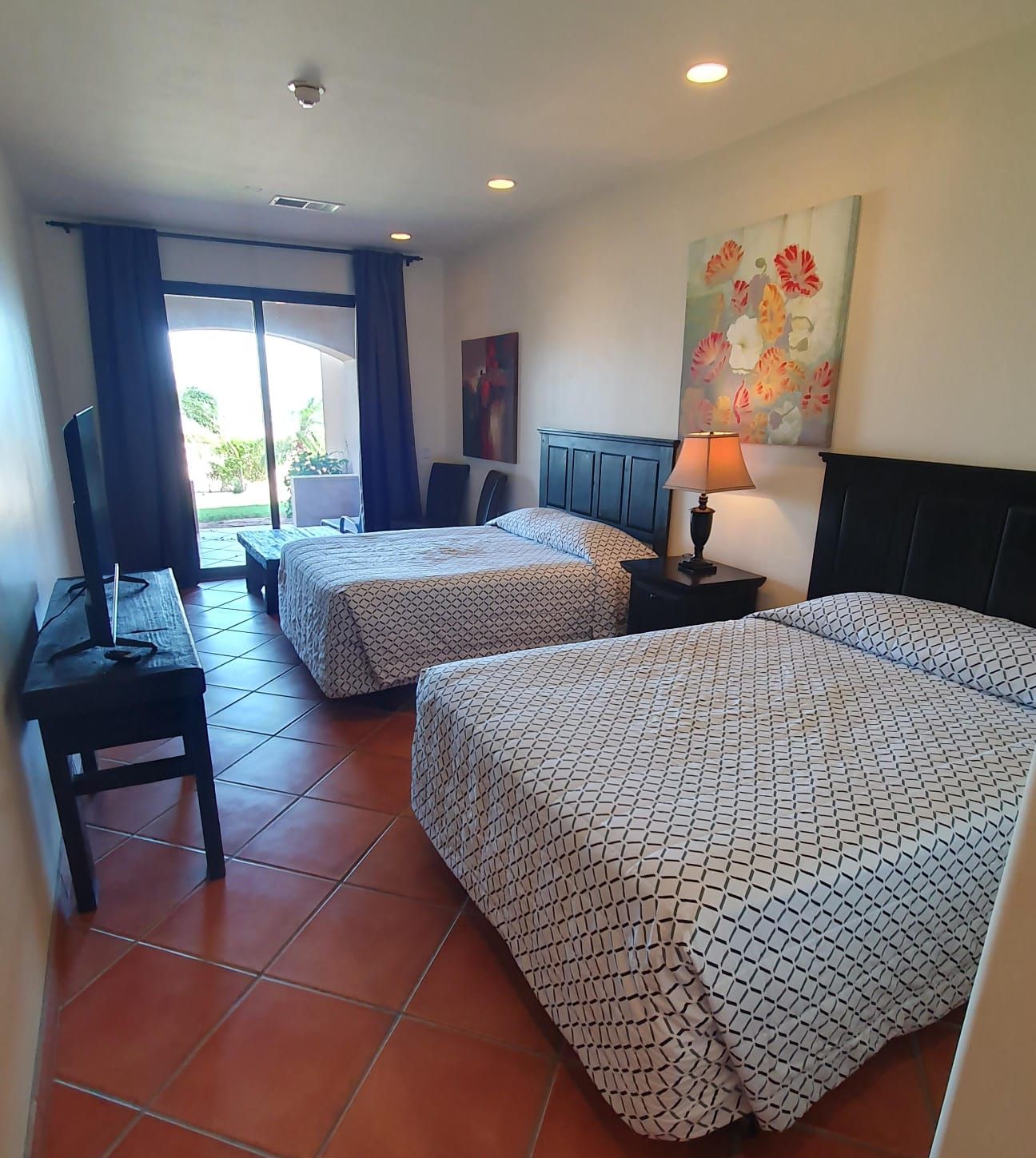 Habitación de hotel con dos camas, un escritorio, un televisor y un cuadro en la pared.