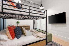 Een stapelbed met een aan de muur bevestigde televisie, een plant op het nachtkastje en een raam met uitzicht.