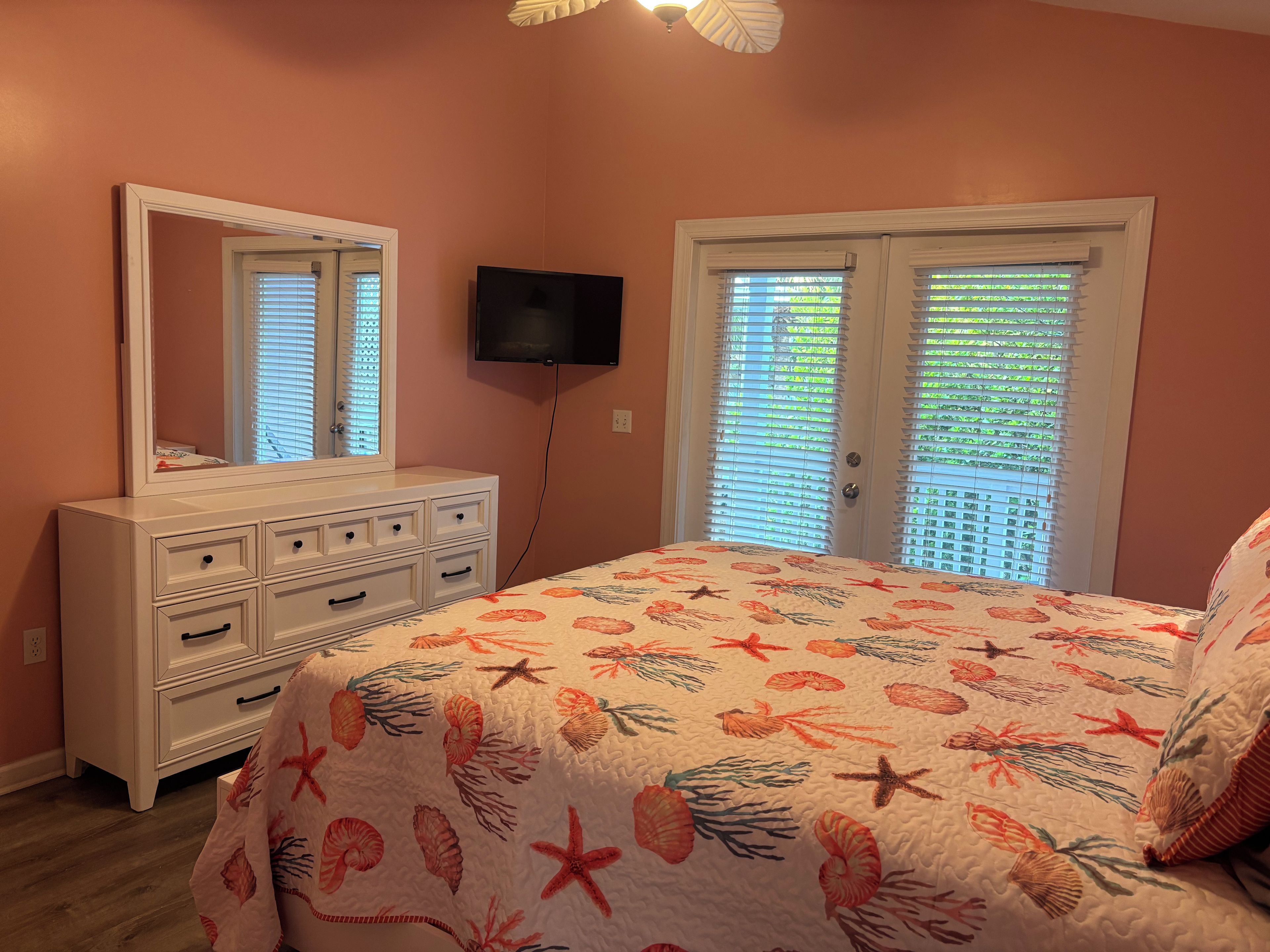 Un dormitorio con cama, cómoda, televisión y ventanas con persianas.
