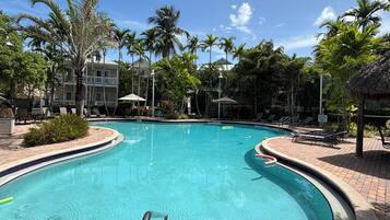 A swimming pool with a curved edge, surrounded by palm trees and lounge chairs.