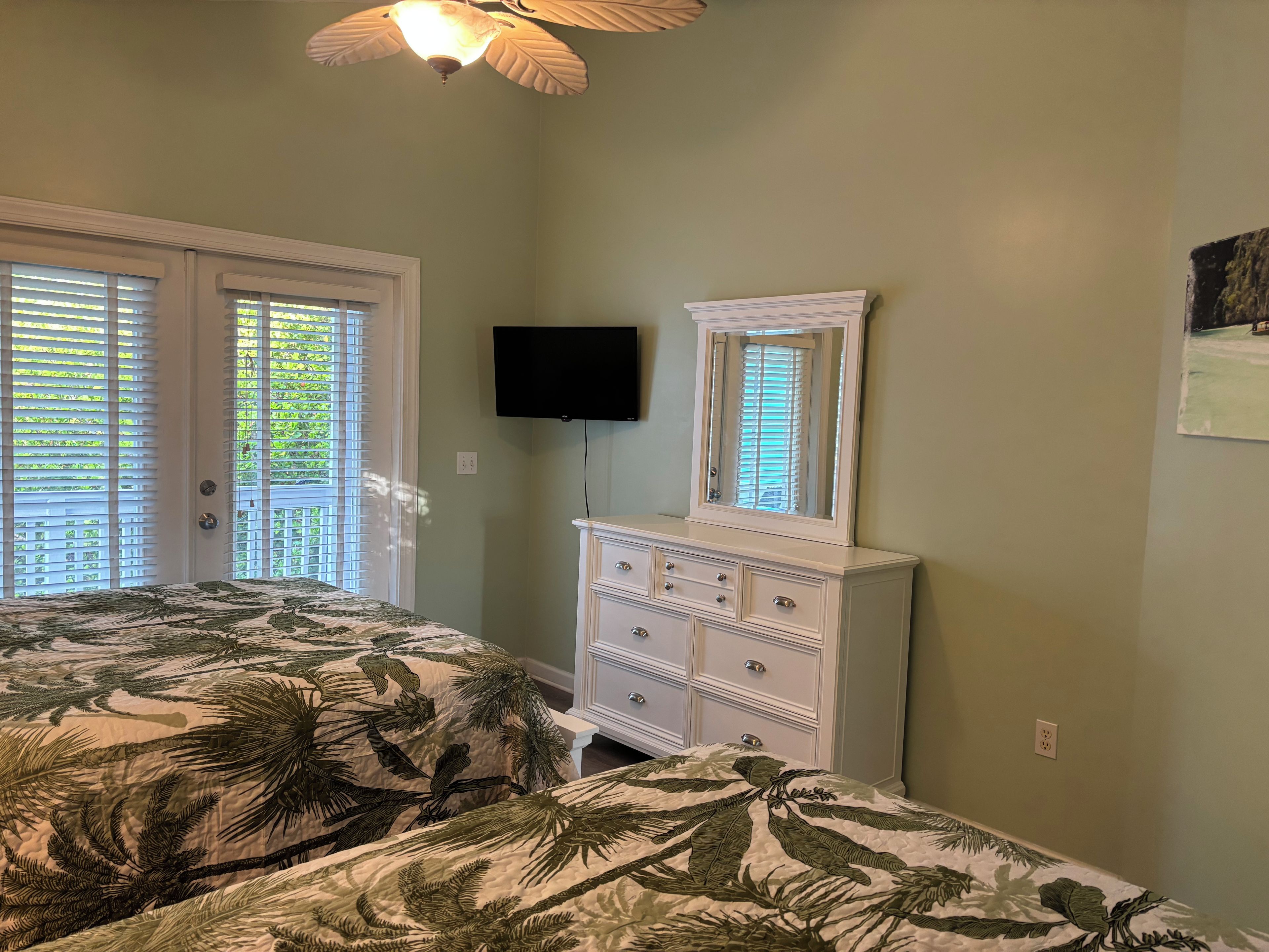 A bedroom with two beds, a dresser, a television, and a ceiling fan.