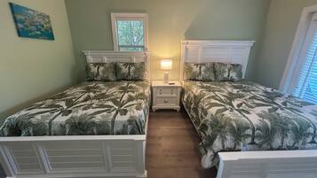 A bedroom with two beds, a nightstand, a lamp, and a window.