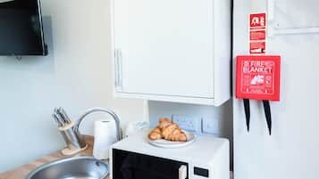 A compact kitchenette with a microwave, a small sink, and a fire blanket mounted on the wall.