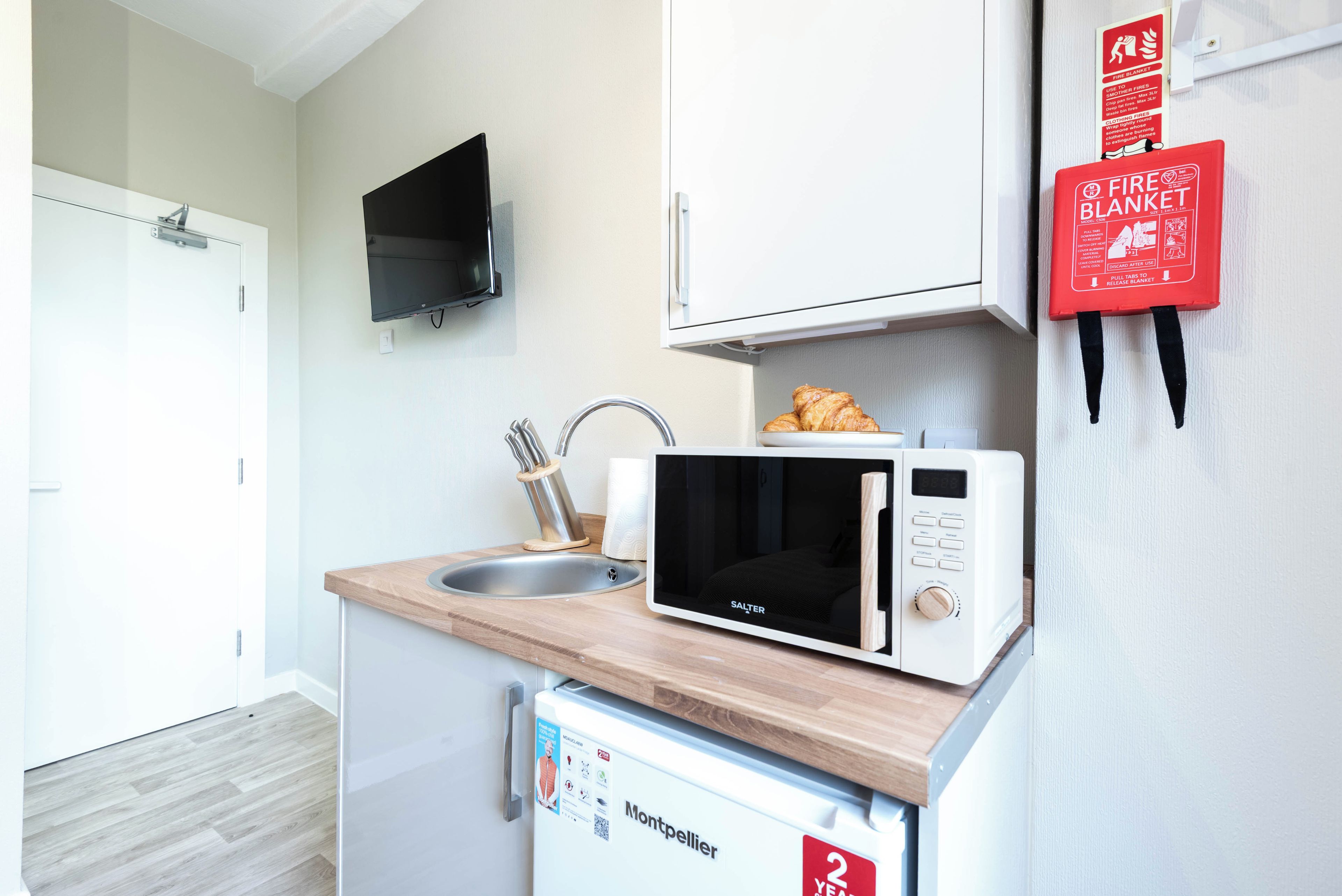 Une petite cuisine équipée d’un four à micro-ondes, d’un évier et d’une couverture anti-feu accrochée au mur.