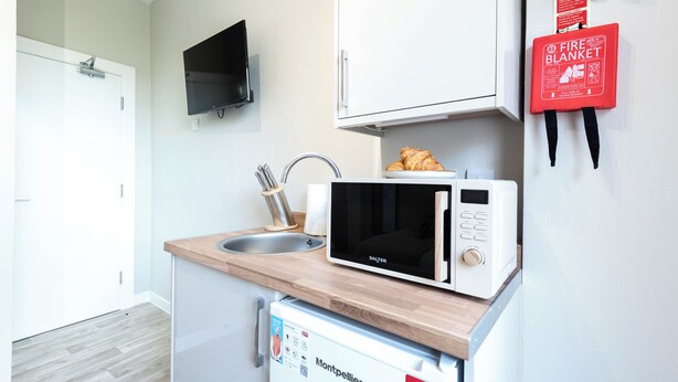 Een compacte kitchenette met een magnetron, een spoelbak en een branddeken aan de muur.