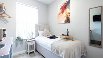 A bedroom with a bed, bedside table, lamp, and a painting on the wall.