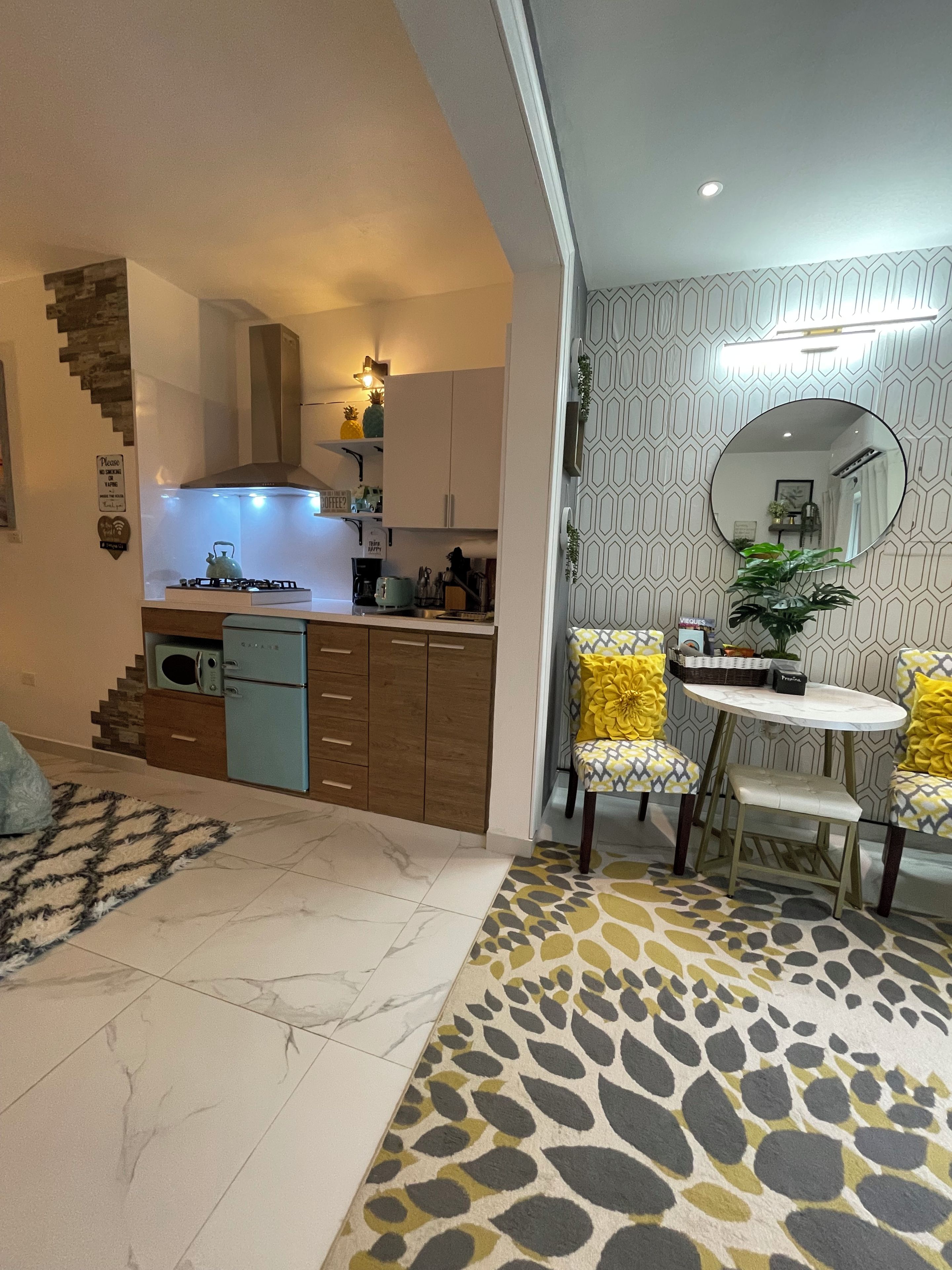 A modern kitchen with a gas stove, microwave, and built-in oven. There is a dining area with a round table and two chairs, and a staircase leading to an upper level.