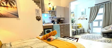 Quarto com cama, pequeno espaço de cozinha e banheiro.