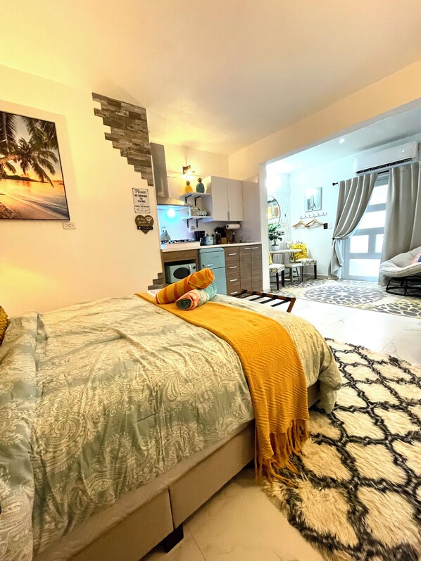 A bedroom with a bed, a small kitchenette, and a bathroom.
