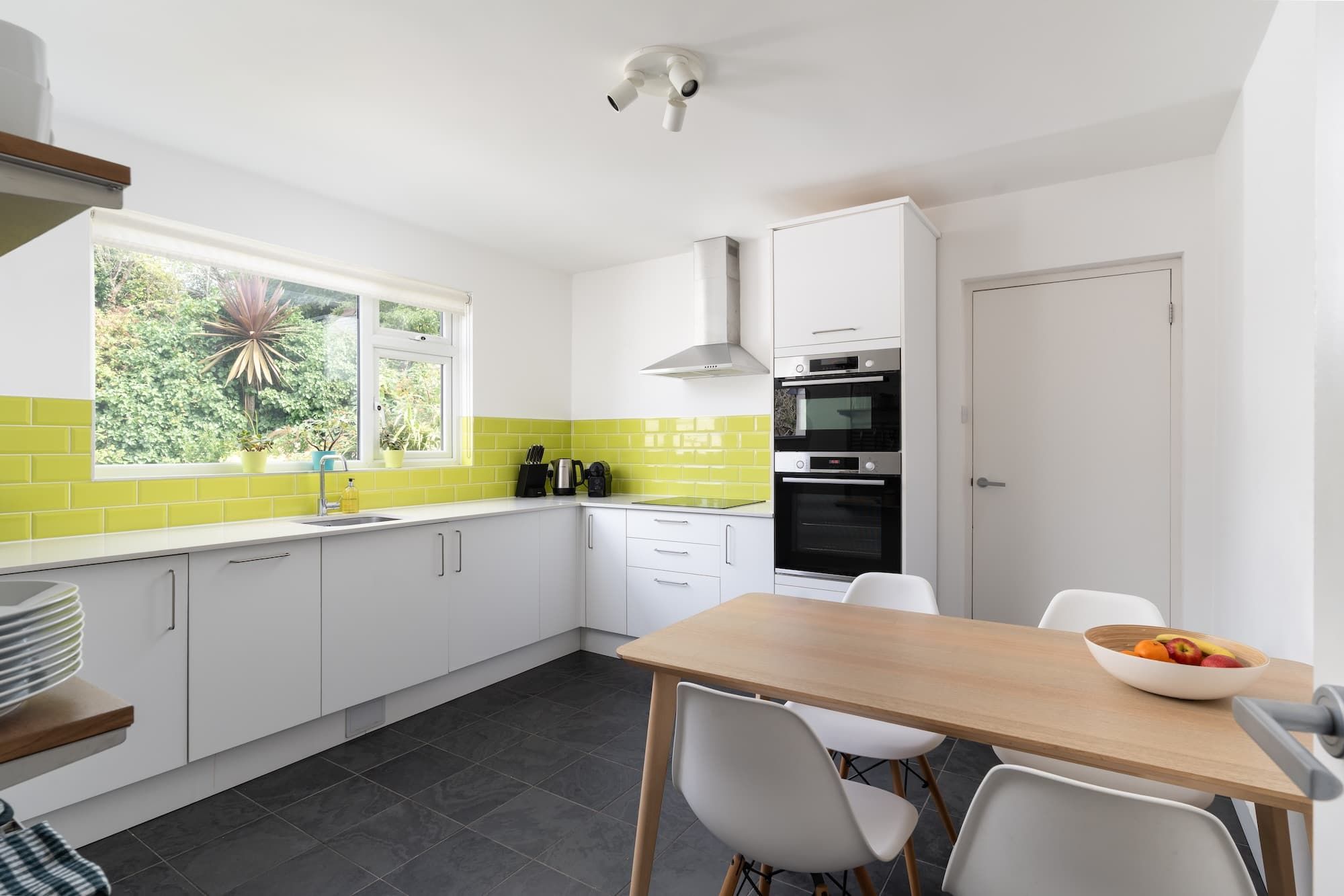 A modern kitchen with white cabinets, a black oven, and a window with a view of greenery.