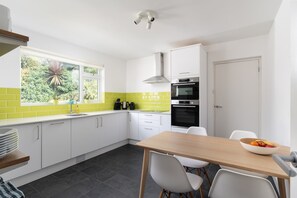 A modern kitchen with white cabinets, a black oven, and a window with a view of greenery. - Modern Home & Garden with Parking, Gorran Haven (Gorran Haven)