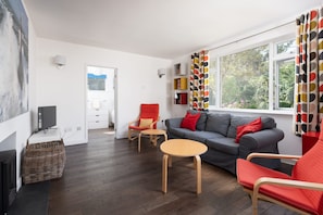 A modern living room with a grey sofa, red chairs, a small wooden table, and a television. - Modern Home & Garden with Parking, Gorran Haven (Gorran Haven)