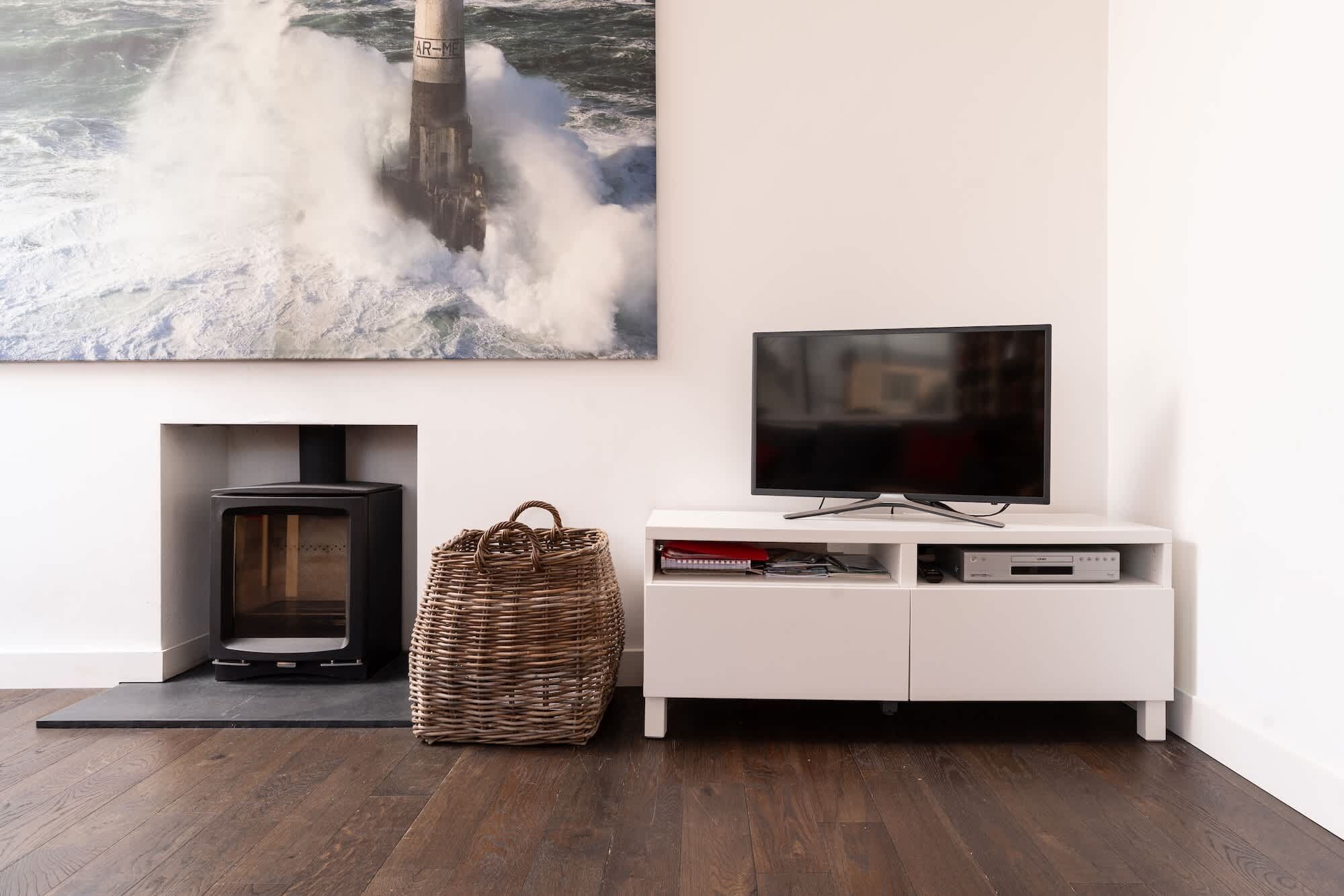 A modern living room with a fireplace, a television on a white cabinet, and a large painting of a lighthouse.