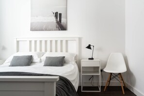 A minimalist bedroom with a bed, bedside table, chair, and a wall-mounted picture. - Modern Home & Garden with Parking, Gorran Haven (Gorran Haven)