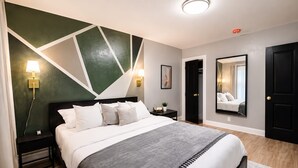 A modern bedroom with a bed, bedside lamps, a nightstand, a mirror, and a door. - Lovely 6-bedroom apartment with AC in vibrant Queens (Queens)