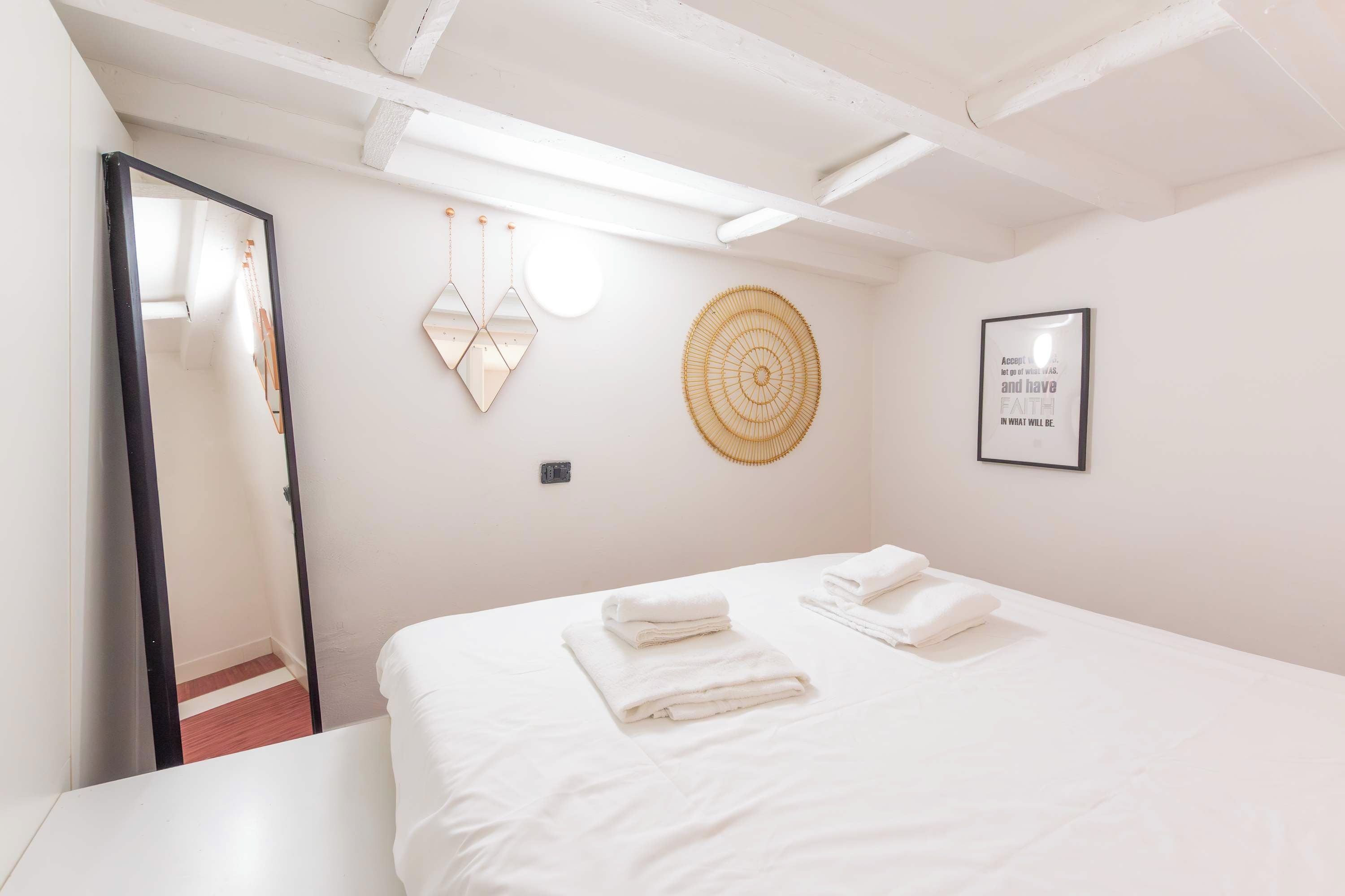 A hotel room with a bed, a mirror, a wall-mounted circular decoration, and a framed inspirational quote.