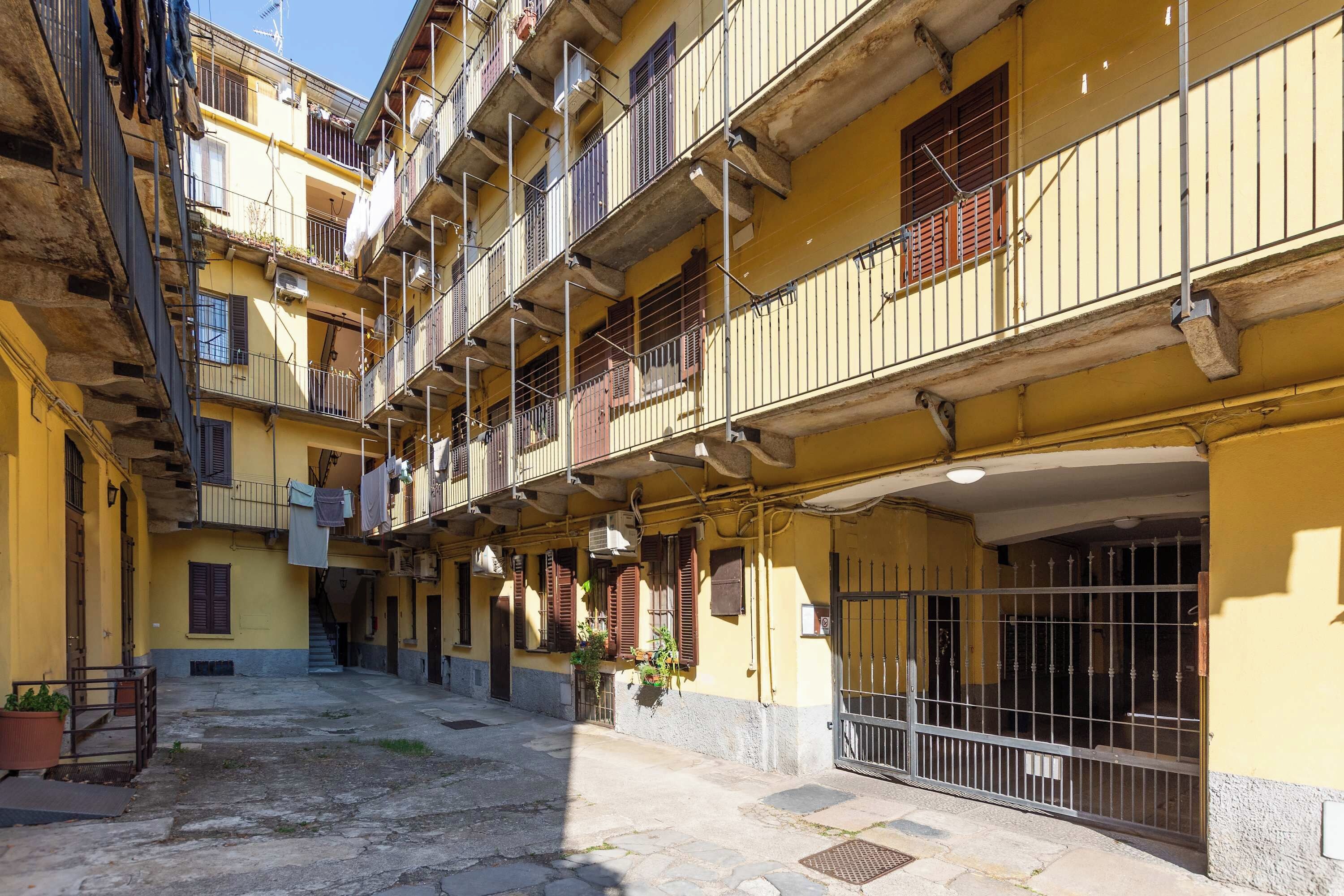 A narrow street with yellow buildings, balconies, and a gated entrance.