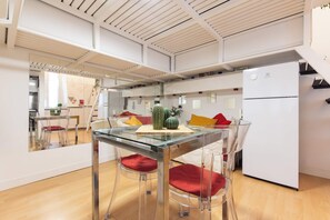 A modern kitchen with a glass dining table, clear chairs, and a white refrigerator. - Casa Orione – Cozy Loft on the Navigli (Milano)