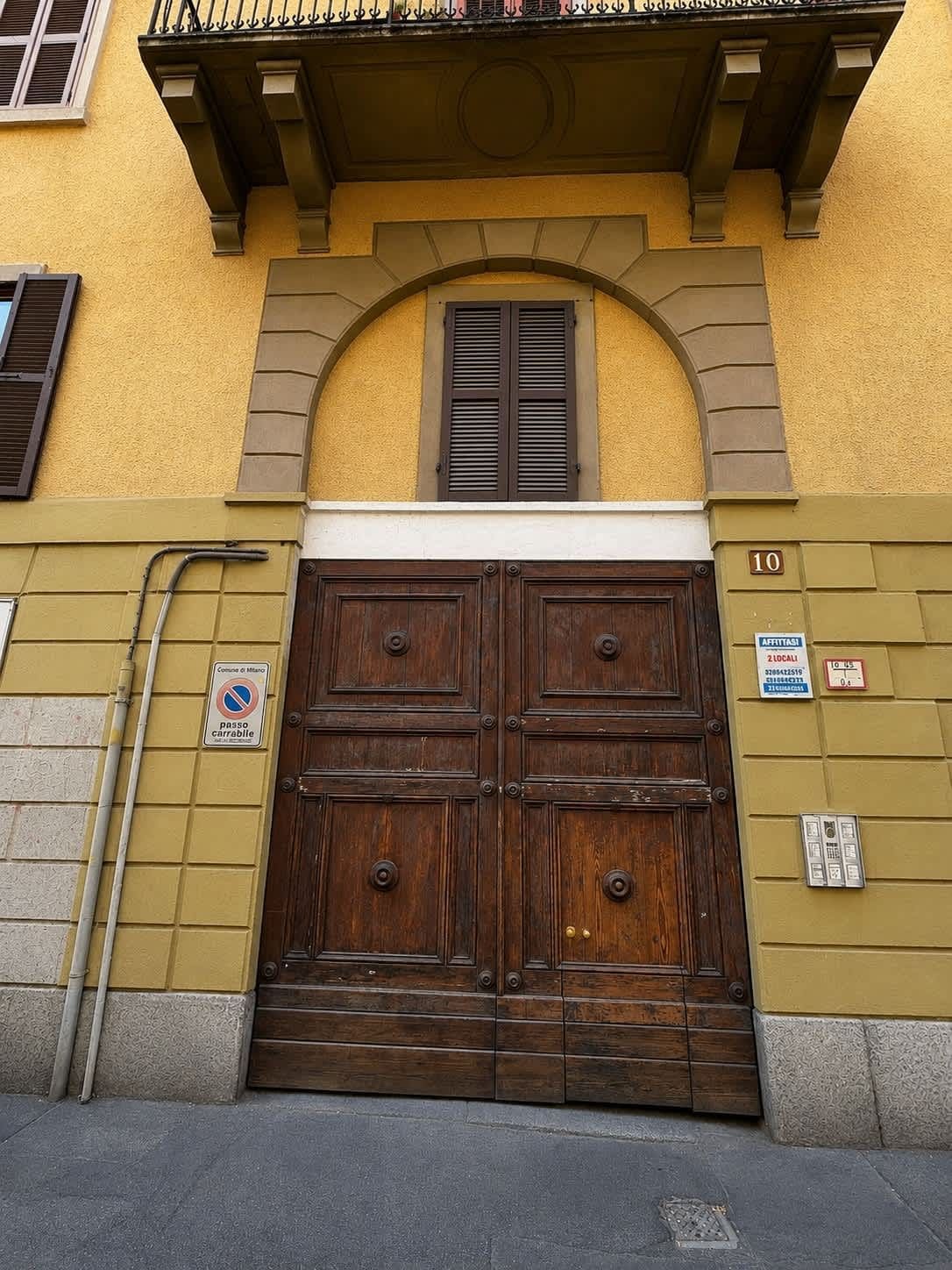 Puerta doble de madera con un balcón superior, un cartel que indica zona prohibida para estacionar y el número de edificio '10'.