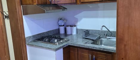 Een keuken met houten kastjes, een roestvrijstalen spoelbak, een gasfornuis en een afvalbak.