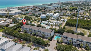 A coastal residential area with a large hotel featuring multiple-story buildings, a swimming pool, and a view of the ocean. - The Coastal Drift - Communal Pool (Miramar Beach)