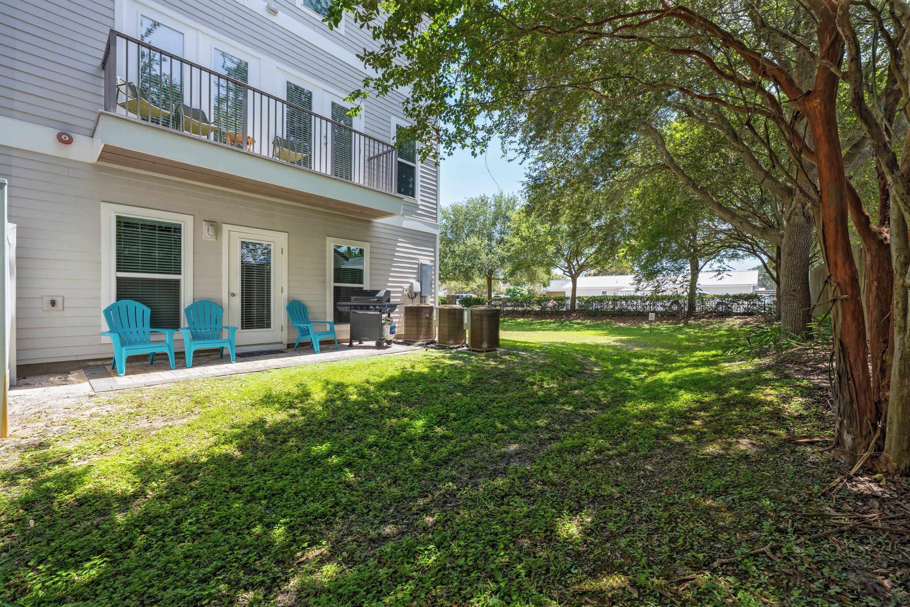 A two-story house with a covered patio area, outdoor seating, and a large tree providing shade.