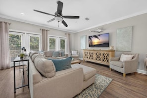 A spacious living room with a ceiling fan, a large flat-screen TV, and a wooden cabinet. - The Coastal Drift - Communal Pool (Miramar Beach)
