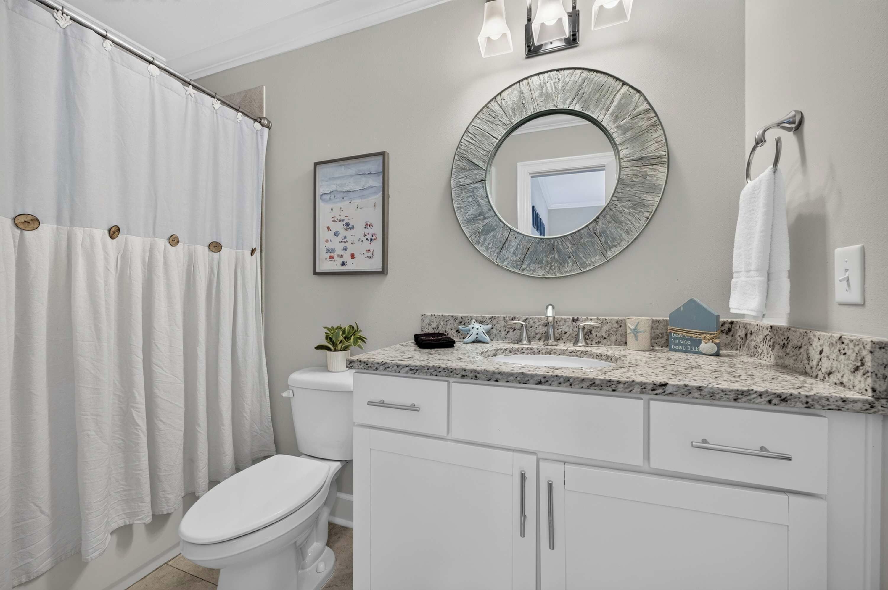 A bathroom with a white toilet, a shower curtain, a sink with a granite countertop, and a mirror with a distressed frame.