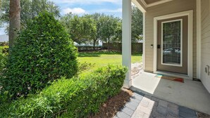 A covered porch with a door, a small garden area with various plants, and a clear sky. - The Coastal Drift - Communal Pool (Miramar Beach)
