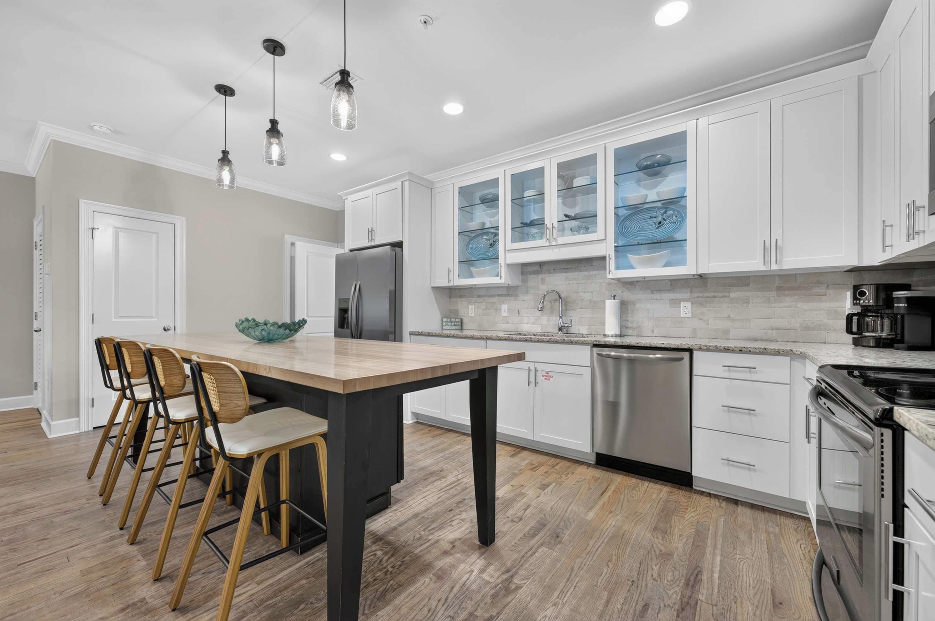 A modern kitchen with white cabinets, a central island with chairs, stainless steel appliances, and pendant lighting.
