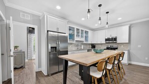 A modern kitchen with a central island, stainless steel appliances, and a dining area with chairs. - The Coastal Drift - Communal Pool (Miramar Beach)