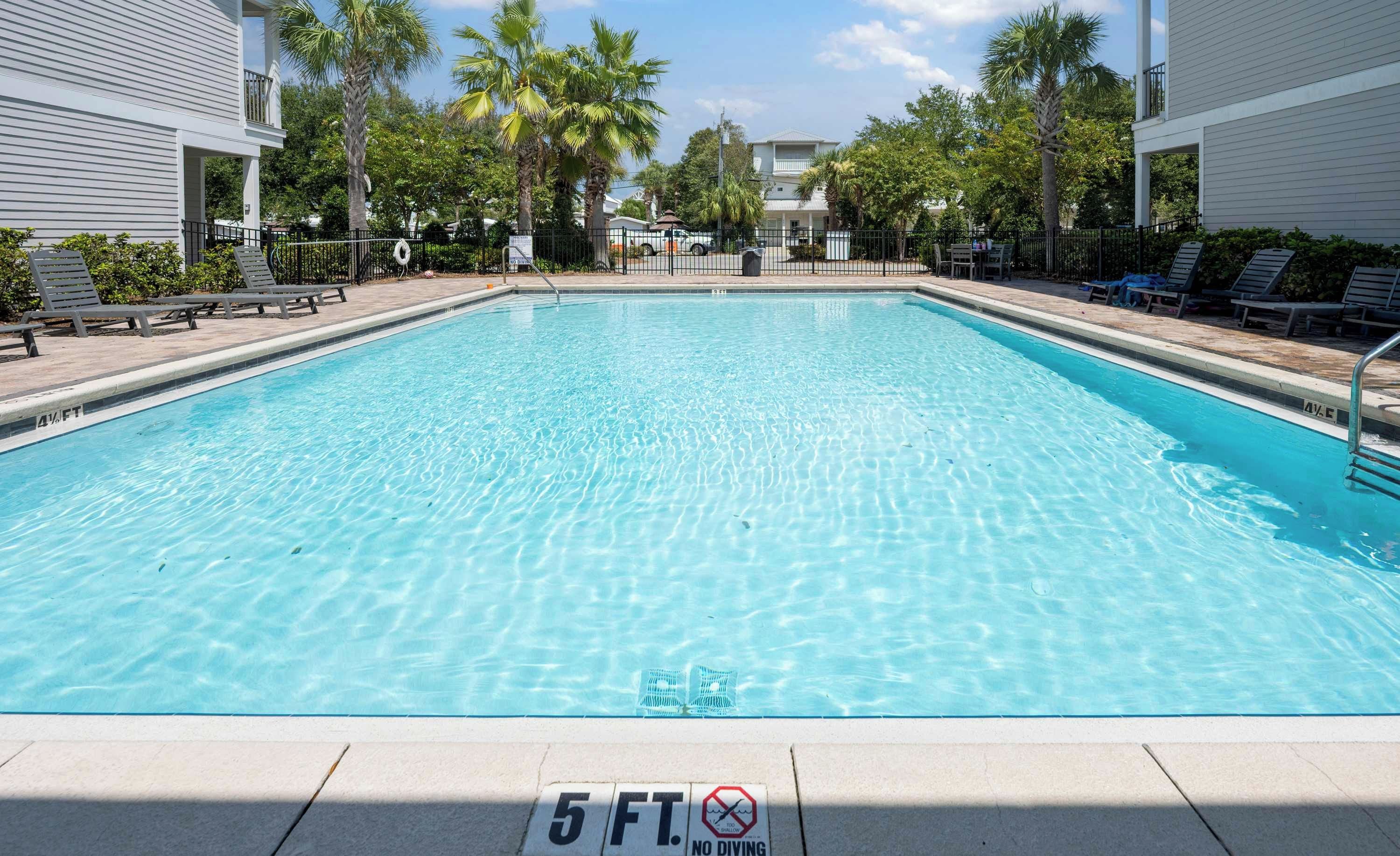 A clear swimming pool with a 5 ft depth marking, surrounded by lounge chairs and palm trees.