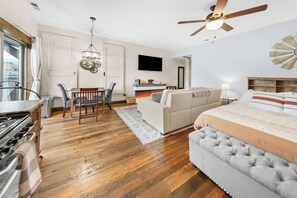 A modern living room with a sofa, a dining area with chairs, a fireplace, a television, and a ceiling fan. - Bliss Retreat - Whitefish Studio (Whitefish)