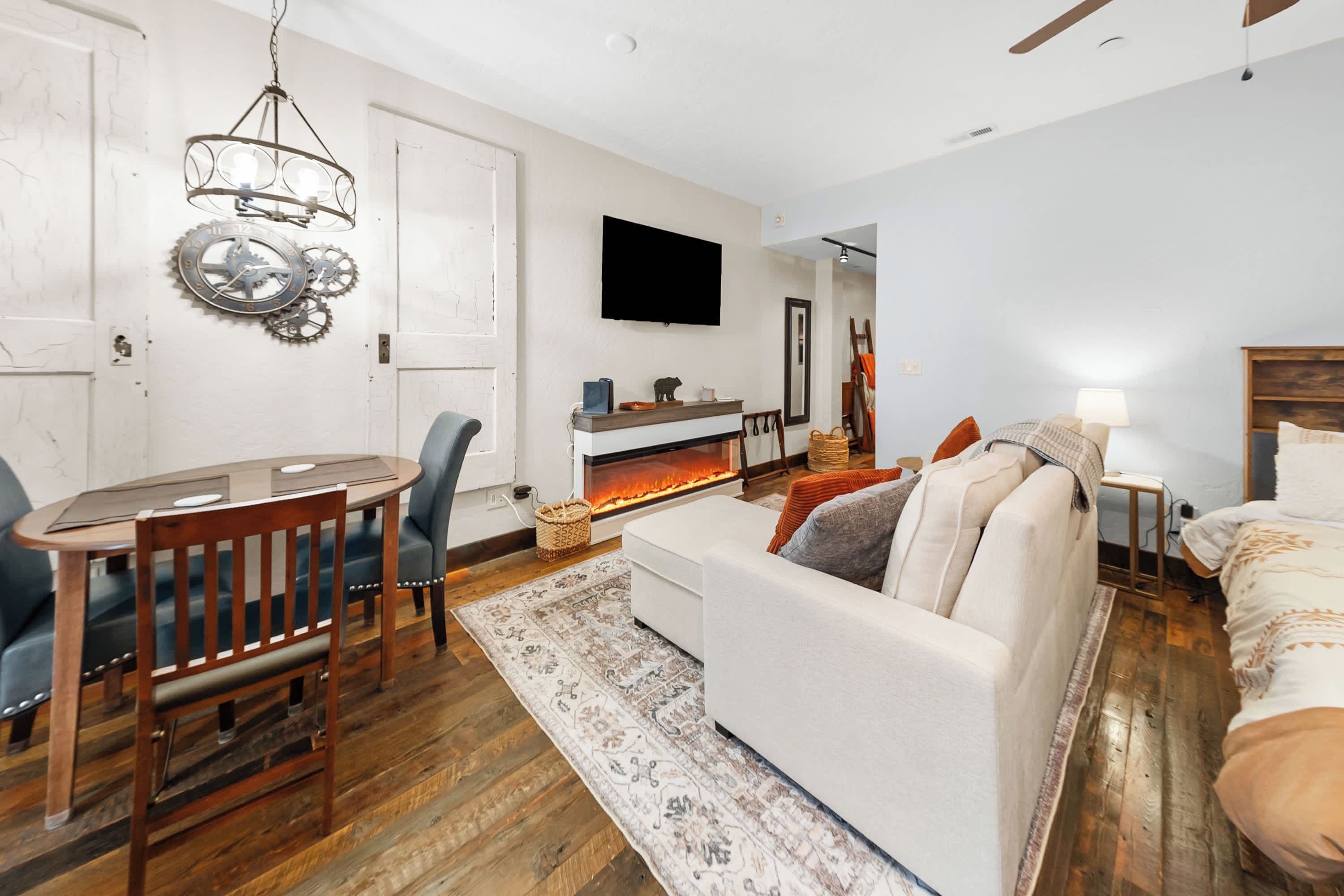 A living room with a fireplace, a television mounted on the wall, and a dining area with a table and chairs.