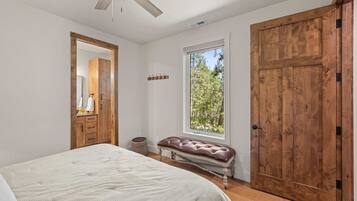 Un dormitorio con cama, un armario de madera, una ventana con vistas a árboles, un ventilador de techo y un perchero en la pared.
