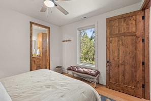 A bedroom with a bed, a wooden wardrobe, a window with a view of trees, a ceiling fan, and a wall-mounted coat rack. - Whitetail Lodge - Rustic Retreat (Eureka)