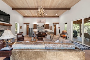 A spacious living room with a large sectional sofa, a fireplace, and a dining area with a kitchen in the background. - Whitetail Lodge - Rustic Retreat (Eureka)