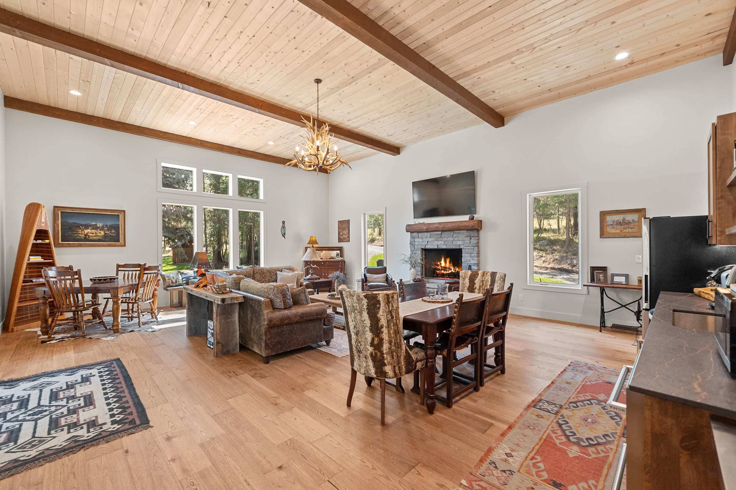 A spacious living room with a fireplace, wooden ceiling, and large windows.