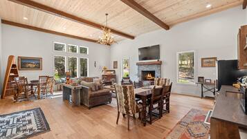 A spacious living room with a fireplace, wooden ceiling, and large windows.