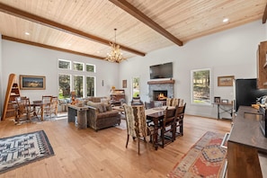 A spacious living room with a fireplace, wooden ceiling, and large windows. - Whitetail Lodge - Rustic Retreat (Eureka)