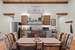 A kitchen with wooden cabinets, a refrigerator, a microwave, and a dining table with chairs. - Whitetail Lodge - Rustic Retreat (Eureka)