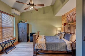 A bedroom with a bed, a ceiling fan, a dresser, a radiator, and a painting on the wall.