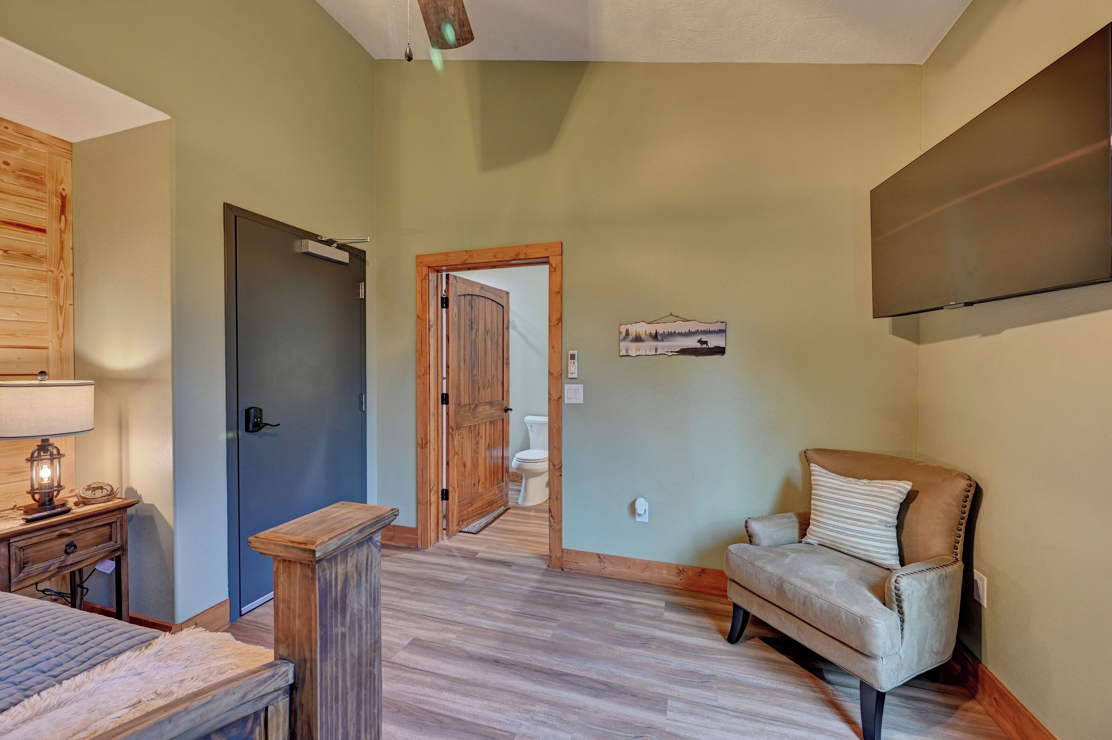 A room with a bed, a chair, a wooden cabinet, a door, and a wall-mounted TV.