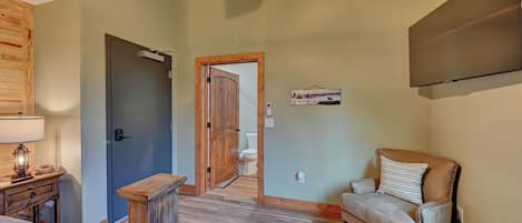 A room with a bed, a chair, a wooden cabinet, a door, and a wall-mounted TV.