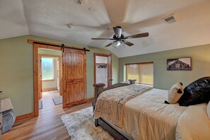 Une chambre à coucher avec un lit, un ventilateur de plafond, une porte en bois et une fenêtre avec des stores.