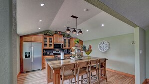 A modern kitchen with wooden cabinets, a stainless steel refrigerator, a microwave, and a dining area with a wooden table and chairs. - Rustic-Chic Barn with 4-Private Suites, 3-upstairs BR's made for Family memories (Montgomery)