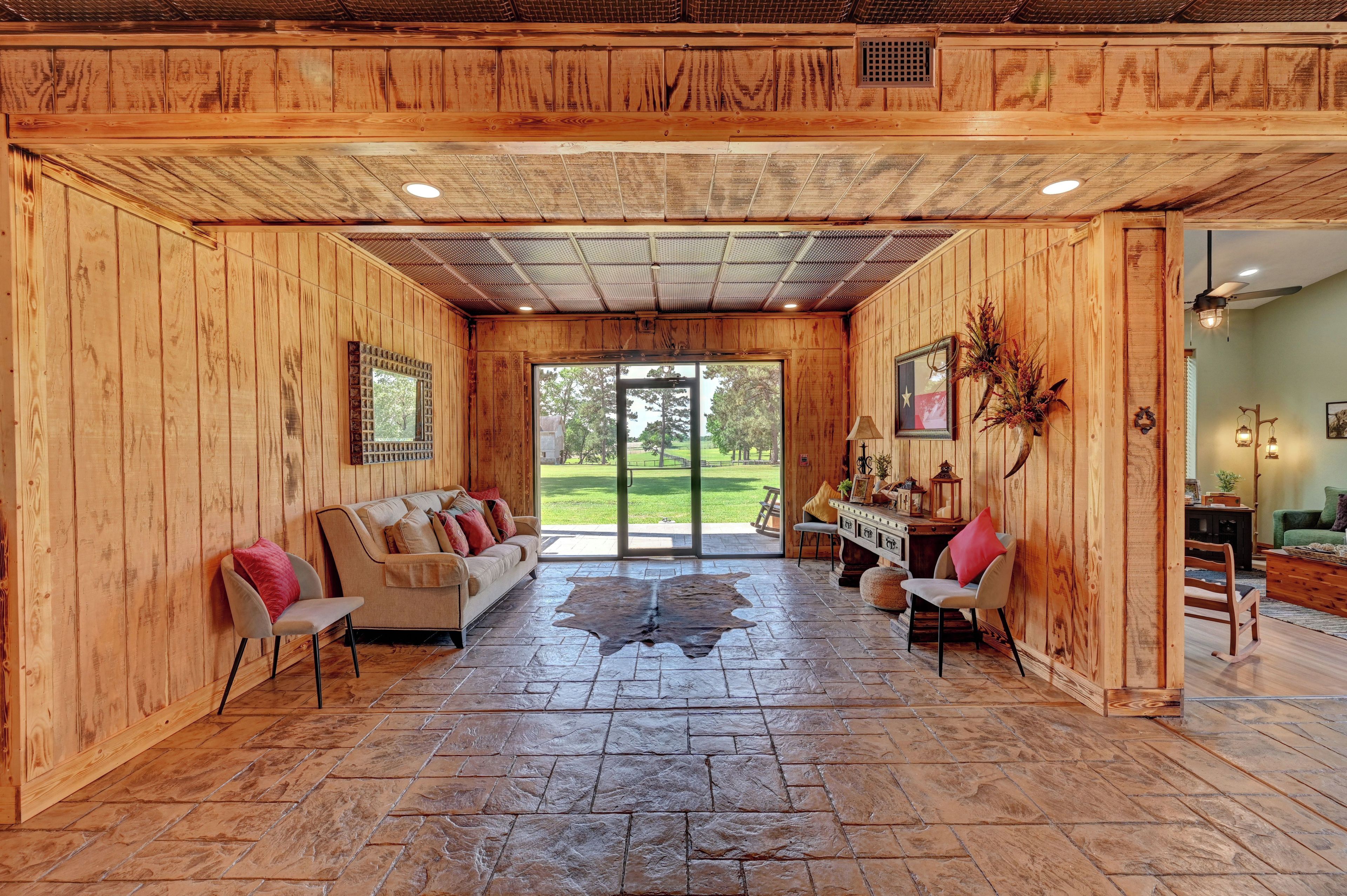 A spacious room with a stone floor, wooden walls, a large window, and a view of the outdoors.
