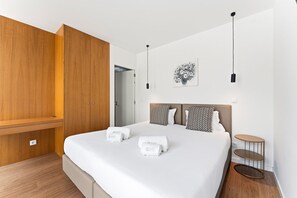 A modern bedroom with a large bed, wooden wardrobe, and a small round table. - GuestReady - PoetikBlue - Studio 2 (Porto)