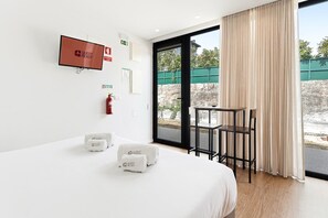A hotel room with a bed, a television, a fire extinguisher, and a view of the outside. - GuestReady - PoetikBlue - Studio 2 (Porto)
