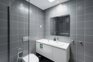 A modern bathroom with a white sink, a mirror, and a shower enclosure. - GuestReady - PoetikBlue - Studio 2 (Porto)